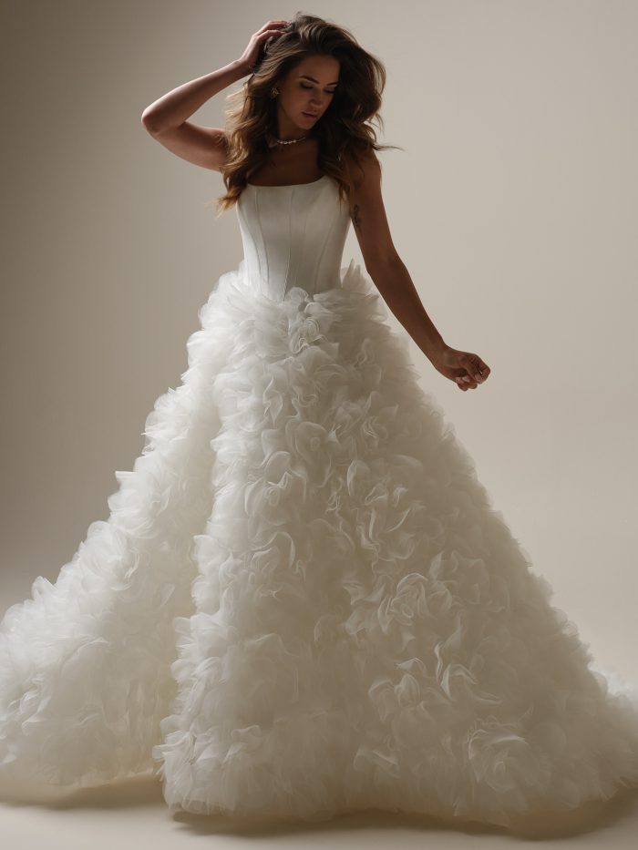 Model wearing Sottero and Midgley Ross ballgown wedding dress with a square neckline, structured bodice, and voluminous organza skirt adorned with 3D floral ruffles.