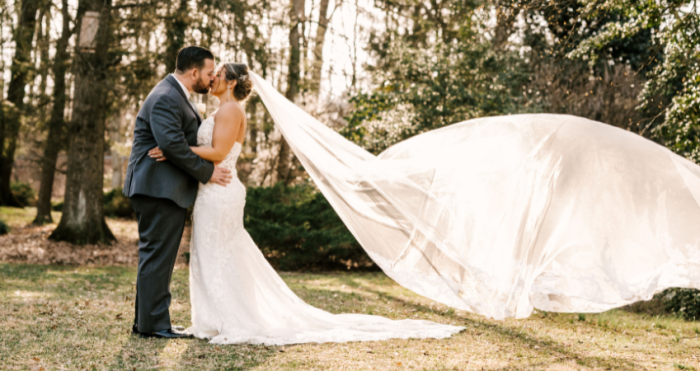 Bride and groom sharing a kiss outdoors with a long flowing veil captured mid-air.