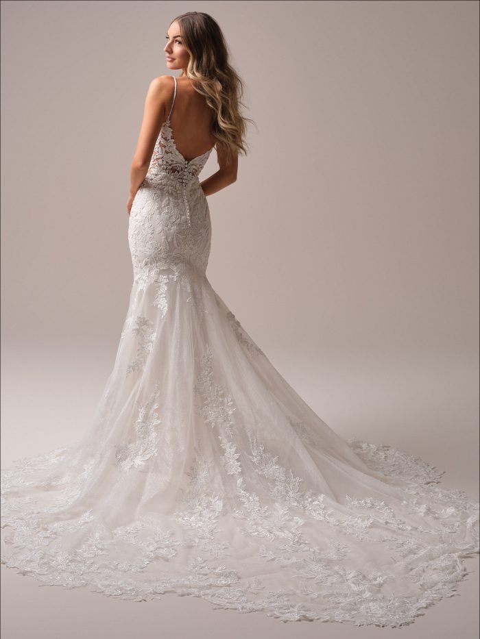 Back view of a lace fit-and-flare wedding dress with beaded spaghetti straps, a low illusion back, and a dramatic chapel-length train adorned with floral lace appliqués.