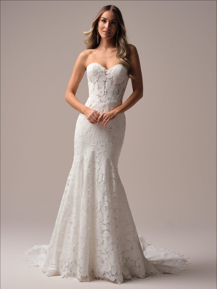 Full-length view of a bride wearing a strapless fit-and-flare wedding dress with a sweetheart neckline, floral lace overlay, and chapel train.
