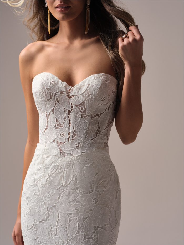 Close-up of a strapless fit-and-flare wedding dress featuring a sweetheart neckline and bold floral lace motifs over sheer illusion bodice.