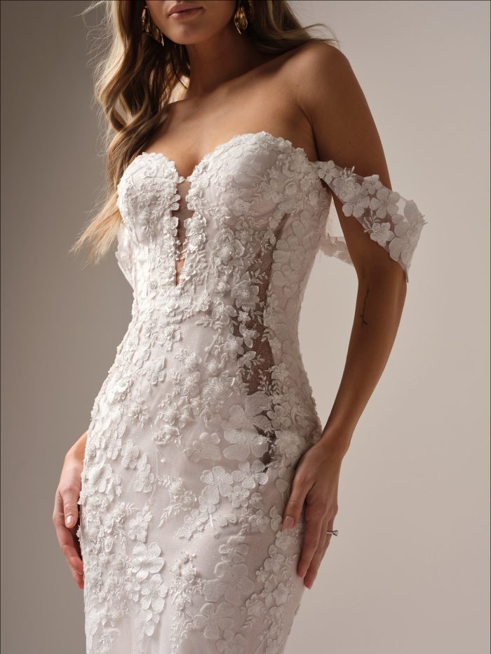 Bride wearing a strapless fit-and-flare wedding gown featuring 3D floral lace appliqués and off-the-shoulder illusion straps, with a plunging illusion neckline and side cutouts.