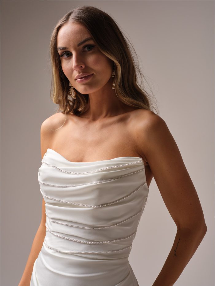 Close-up of a strapless sheath wedding dress with a draped satin bodice featuring delicate topstitched detailing for a textured, modern look.