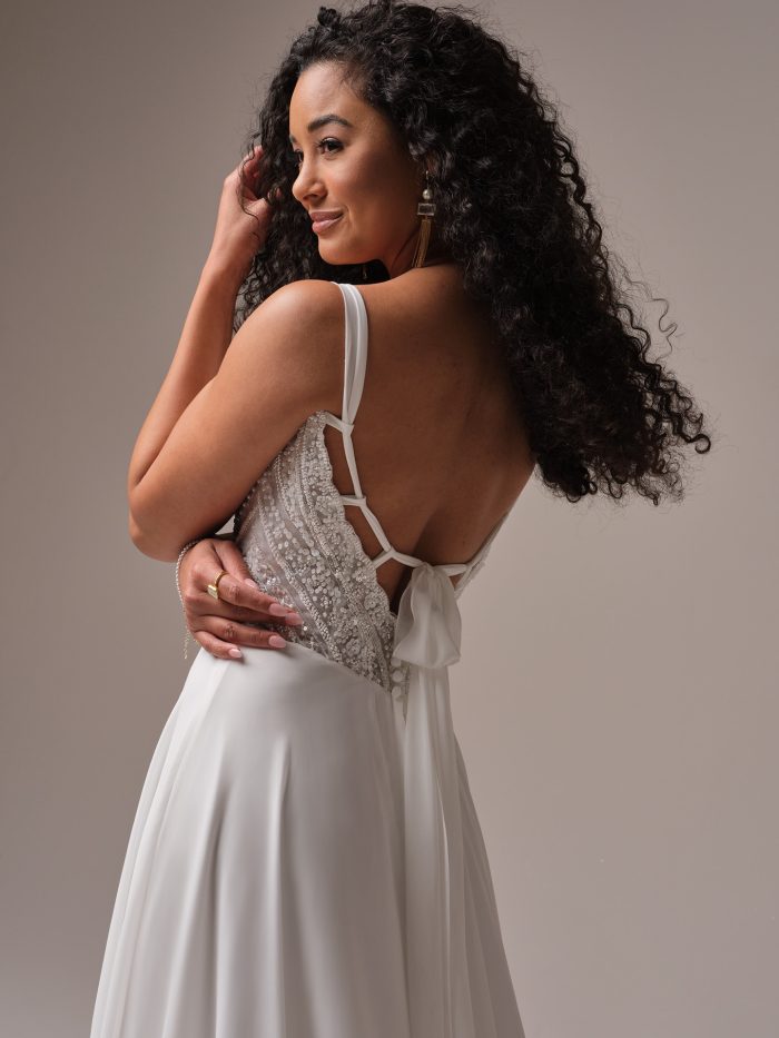 Back view of the Rebecca Ingram Clara gown highlighting the beaded illusion bodice, strappy back with a chiffon bow tie, and lightweight A-line chiffon skirt for an elegant yet effortless finish.
