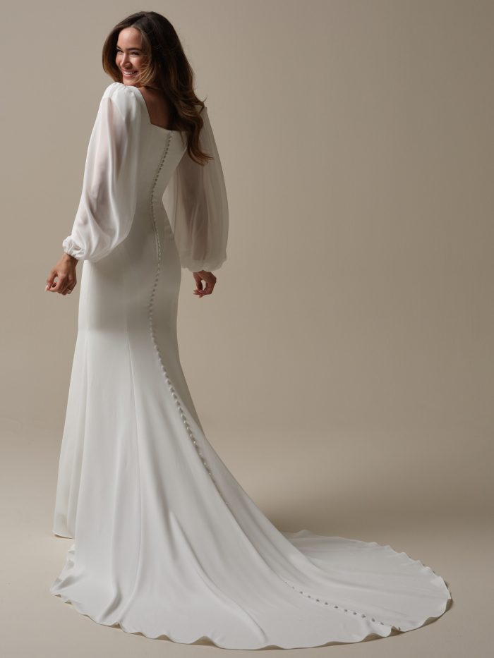 The back view of the bride shows a row of fabric-covered buttons trailing down the back of the dress and train, accentuating the clean design and elegant drape of the gown.