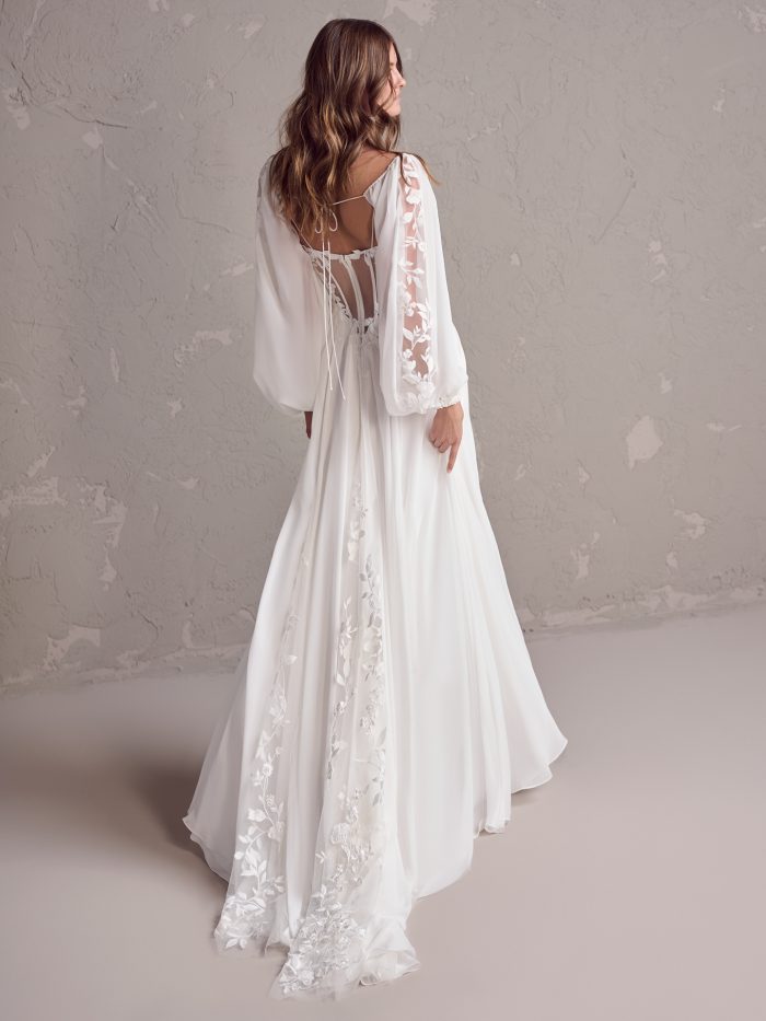 Back view of a sheath wedding dress featuring illusion lace panels, lace-up detail, and floral appliqués trailing down the chiffon skirt and chapel train.