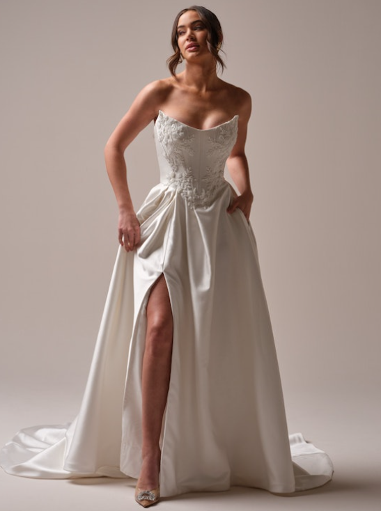 Bride wearing a strapless A-line wedding dress with structured pleating, thigh-high slit, and floral beaded embroidery on the bodice.
