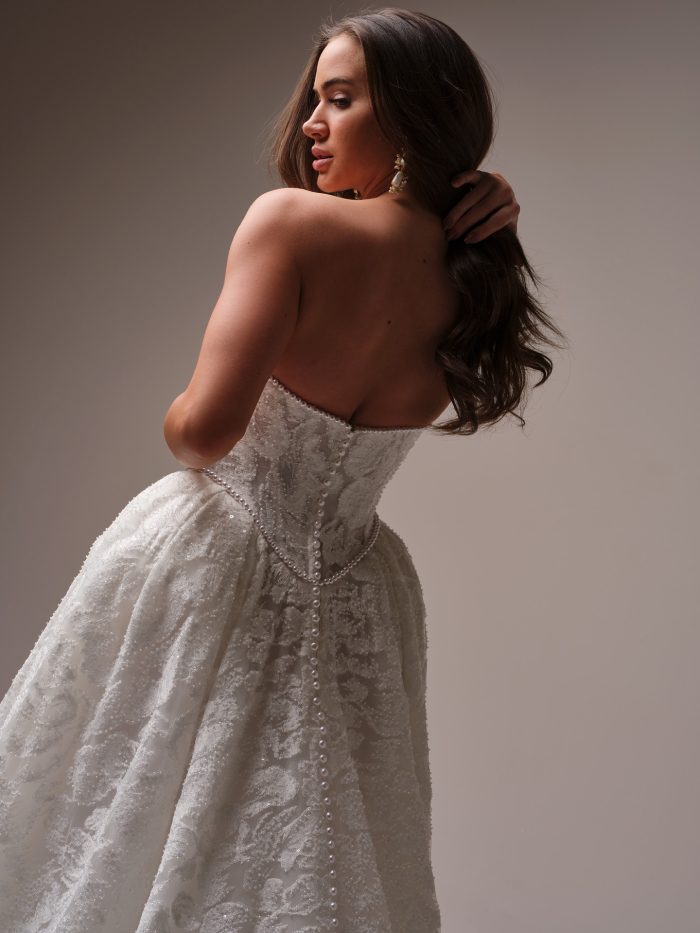 Back view of a strapless ballgown wedding dress with a pearl-trimmed bodice and textured jacquard fabric, featuring a row of pearls along the back seam.