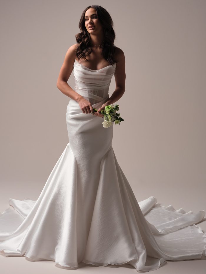 Front view of a fit-and-flare wedding dress featuring a sheer ruched bodice with a draped cowl neckline, textured satin skirt, and chapel-length train.