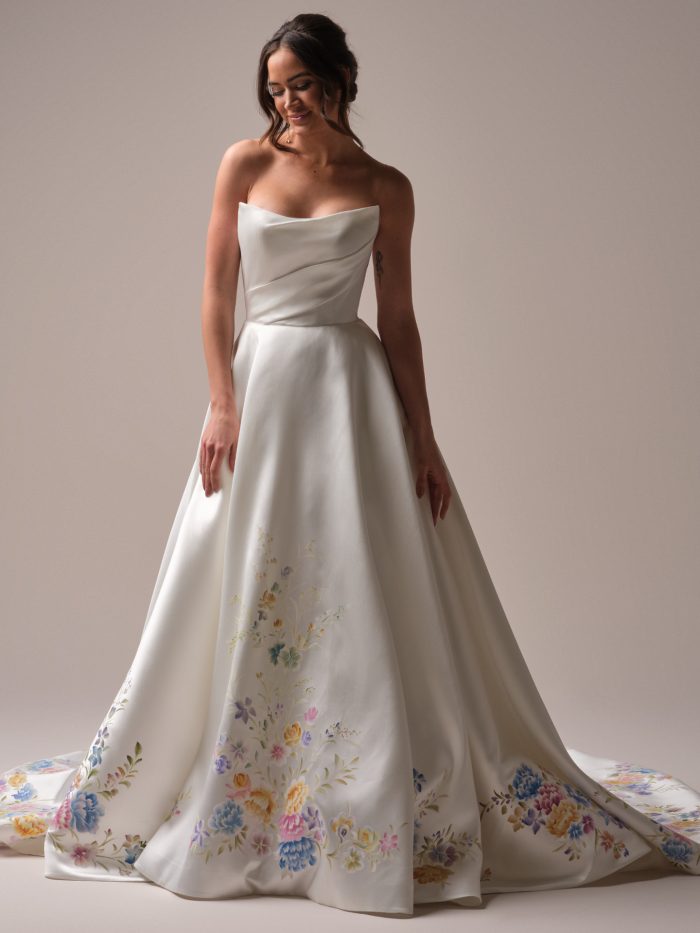 Front view of an A-line wedding dress featuring a strapless draped satin bodice and a full skirt adorned with vibrant hand-painted floral motifs.