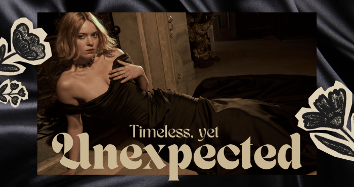 Black satin wedding gown Recine by Sottero and Midgley, styled in a dramatic reclining pose across an ornate interior floor. The off-the-shoulder design features a softly draped neckline, fitted silhouette through the bodice and hips, and a fluid skirt that extends into a long, elegant train. Warm, moody lighting highlights the gown’s lustrous texture against carved architectural details and dark wood accents. Decorative floral illustrations frame the composition, with overlaid text reading “Timeless, yet Unexpected.”