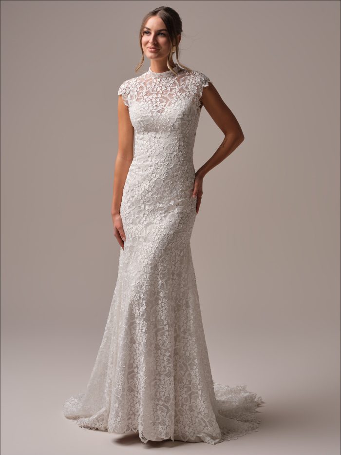 Bride wearing the Maggie Sottero Auburn sheath wedding dress featuring a high illusion neckline, cap sleeves, and allover floral lace with a soft chapel train for a modest yet modern bridal look.