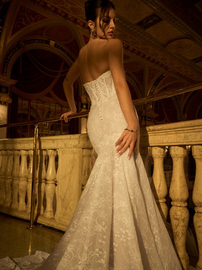 Back view of a bride wearing the Bellevue Royale fit-and-flare wedding dress by Maggie Sottero, showcasing the beaded button-back bodice and sparkling lace trumpet silhouette, on a balcony in an ornate theater.