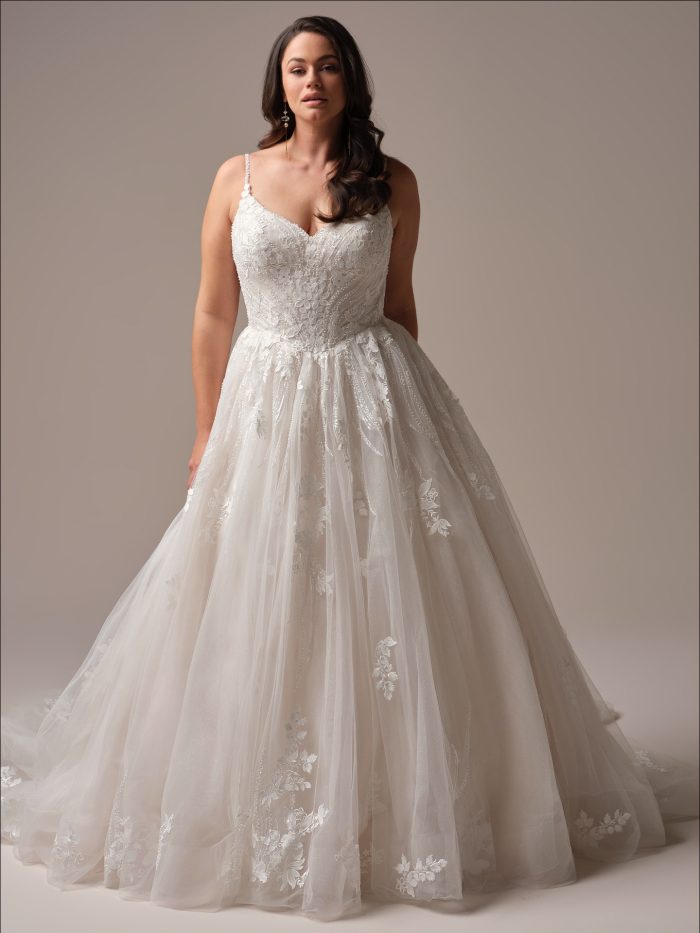 Model wearing Liberty by Maggie Sottero, a ball gown wedding dress with beaded and sequined lace bodice, plunging illusion V-neckline, beaded spaghetti straps, and sparkle tulle skirt.