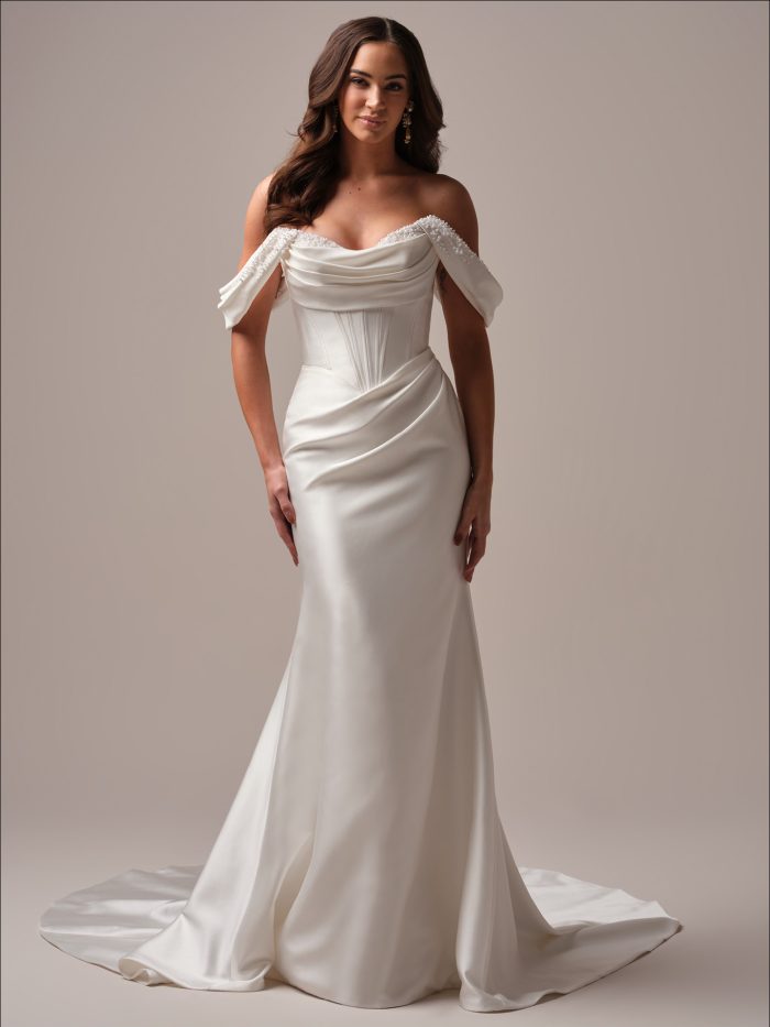 Bride wearing the Maggie Sottero Melissa fit-and-flare wedding dress featuring off-the-shoulder draped sleeves, a structured satin bodice, and a sleek skirt with couture-inspired pleating.