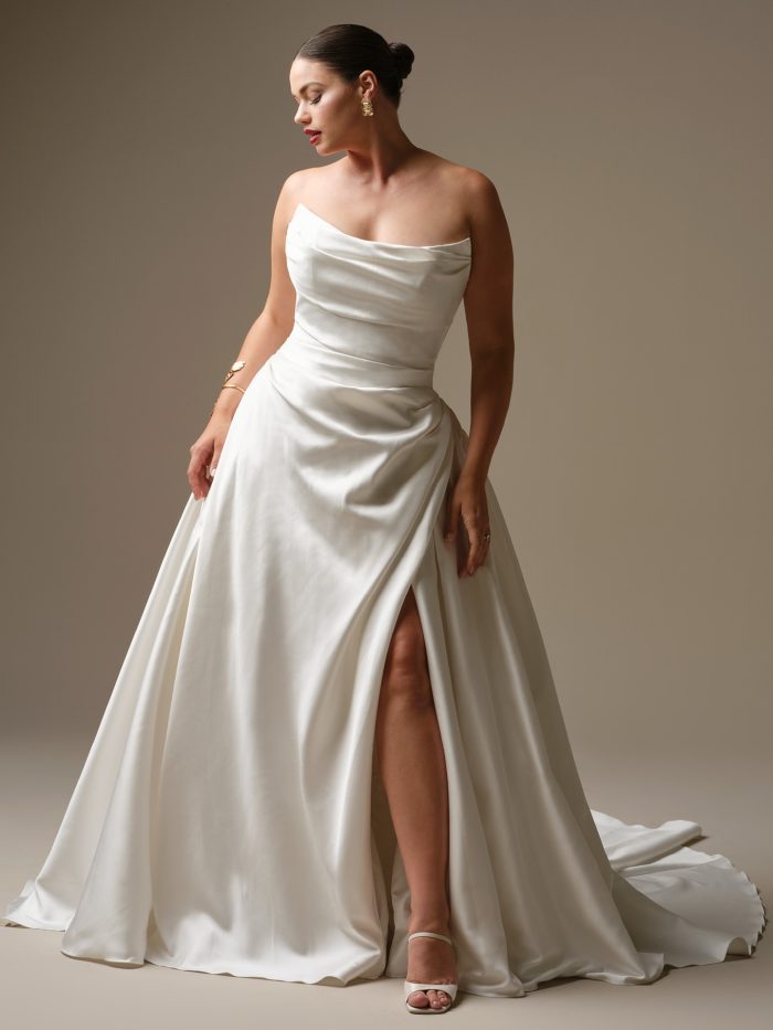 Model wearing Kincaid by Sottero and Midgley, a strapless Cartago satin ball gown wedding dress with asymmetrical draping and a thigh-high slit.