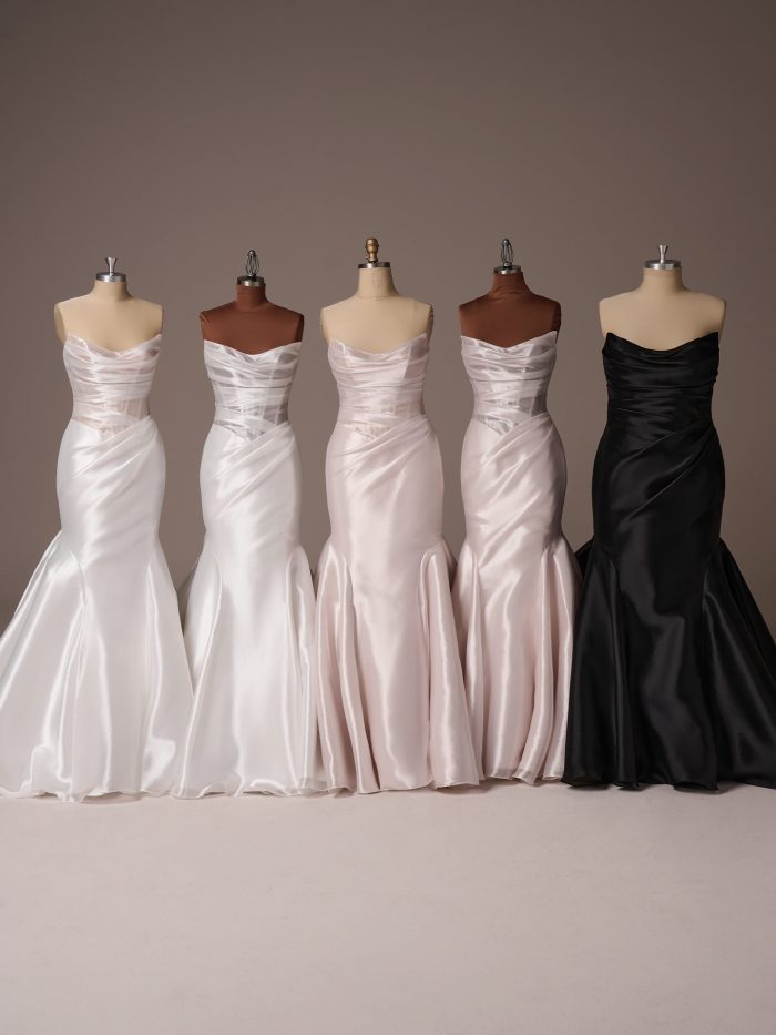 Multiple Lagos fit-and-flare wedding dresses by Sottero and Midgley displayed on mannequins, featuring strapless draped satin bodices with softly structured silhouettes in ivory, blush tones, and black.