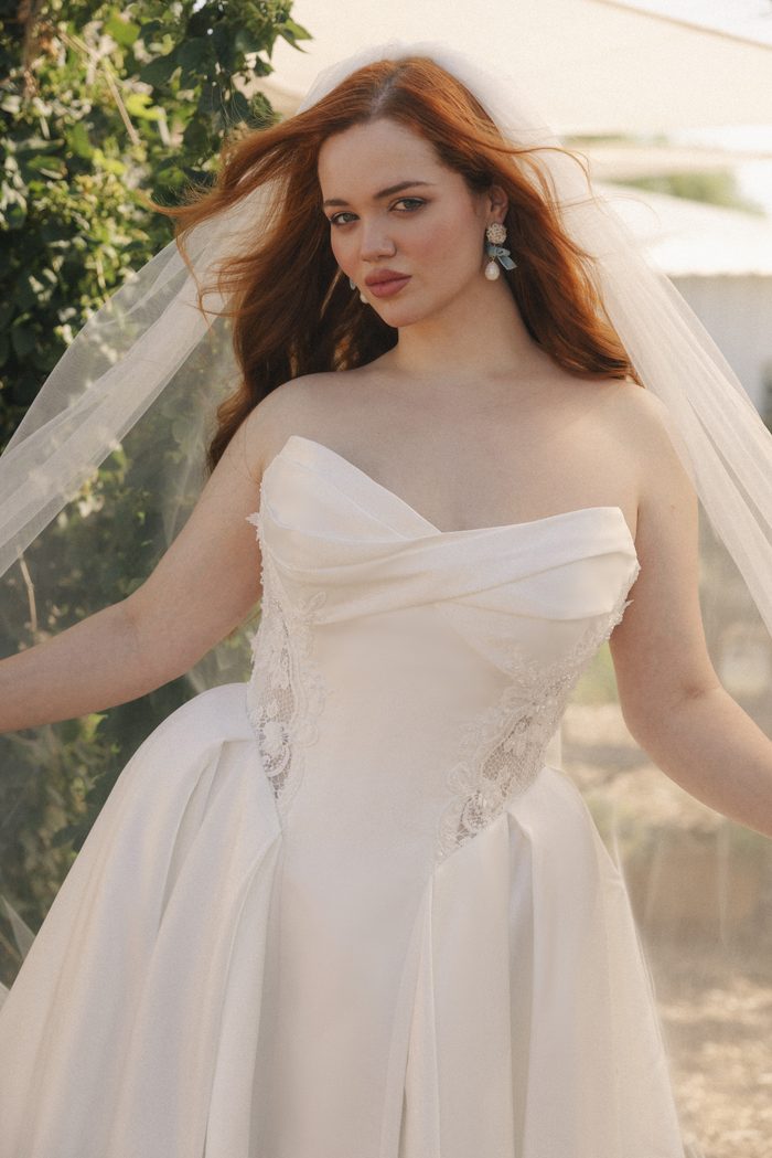 Close-up of the Gigi wedding dress by Rebecca Ingram showcasing a softly draped strapless neckline, lace side panels, and a structured corset bodice paired with a classic bridal veil.