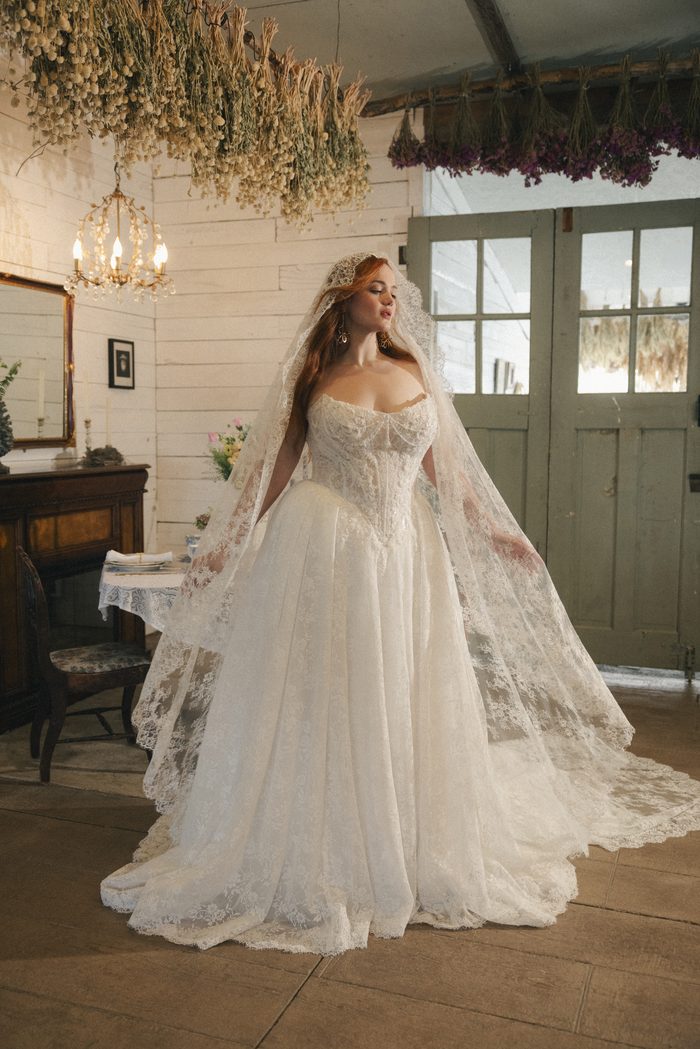 Ryland boho floral wedding dress paired with a lace-edged cathedral veil, featuring a sparkling lace corset bodice, romantic sweetheart neckline, and voluminous A-line skirt in a rustic bridal setting.