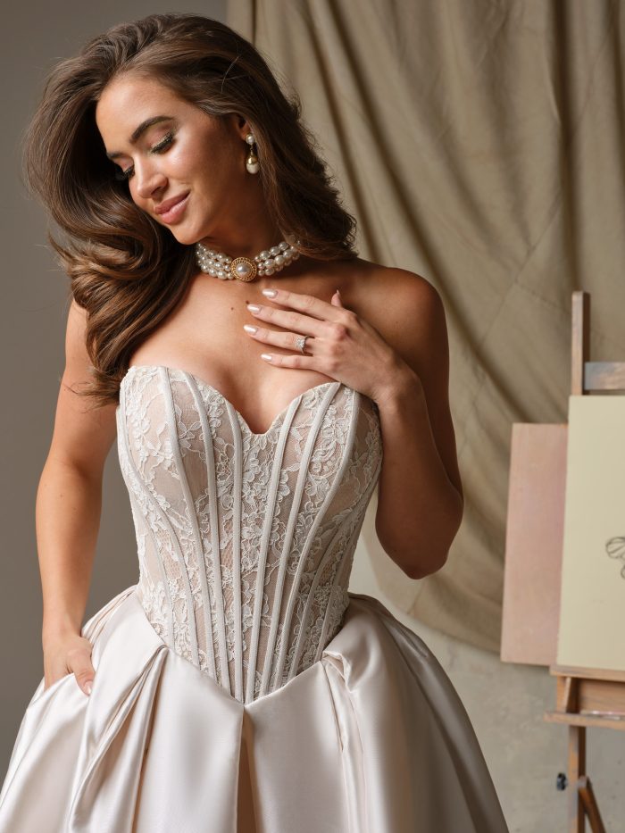 Close-up of  Ashland's strapless lace corset bodice with exposed boning on a satin ballgown wedding dress, paired with layered pearl jewelry and soft glam bridal makeup.