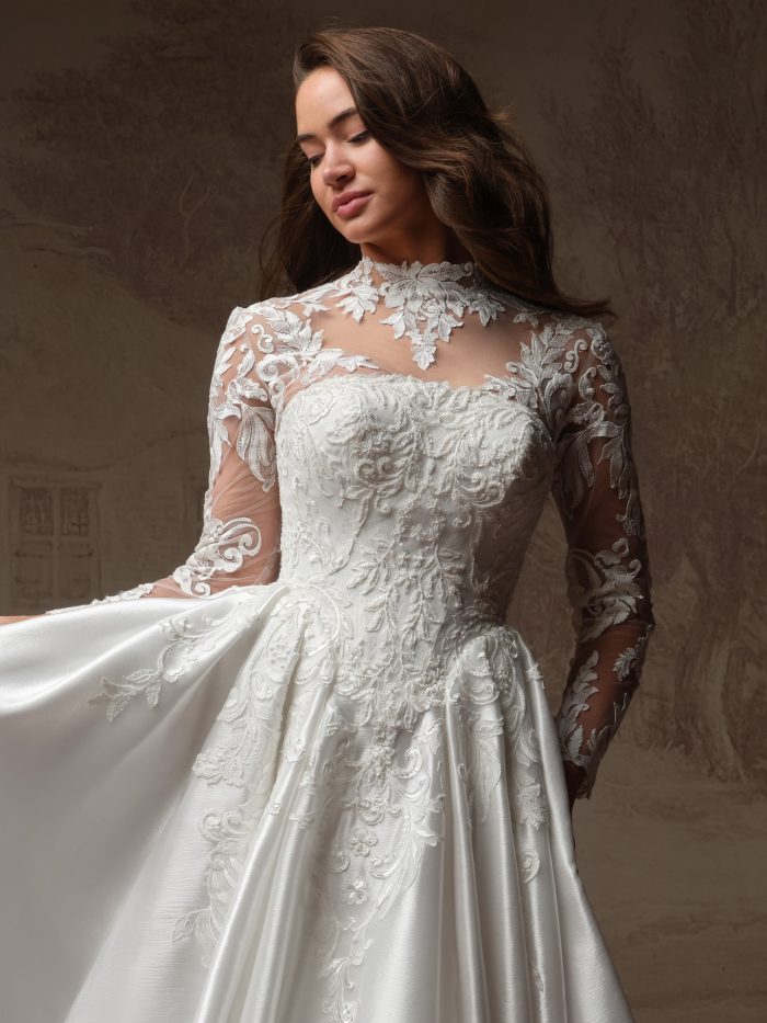Close-up of Maggie Sottero Dahlia wedding dress with a sheer high-neck lace jacket featuring long sleeves and floral appliqué over a structured strapless bodice.