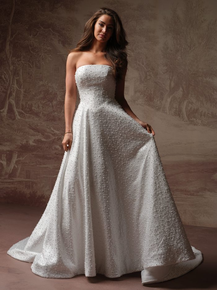 Full-length view of Maggie Sottero Olata A-line wedding gown with a strapless neckline, softly structured bodice, and pearl-studded fabric flowing into a full skirt with subtle train.