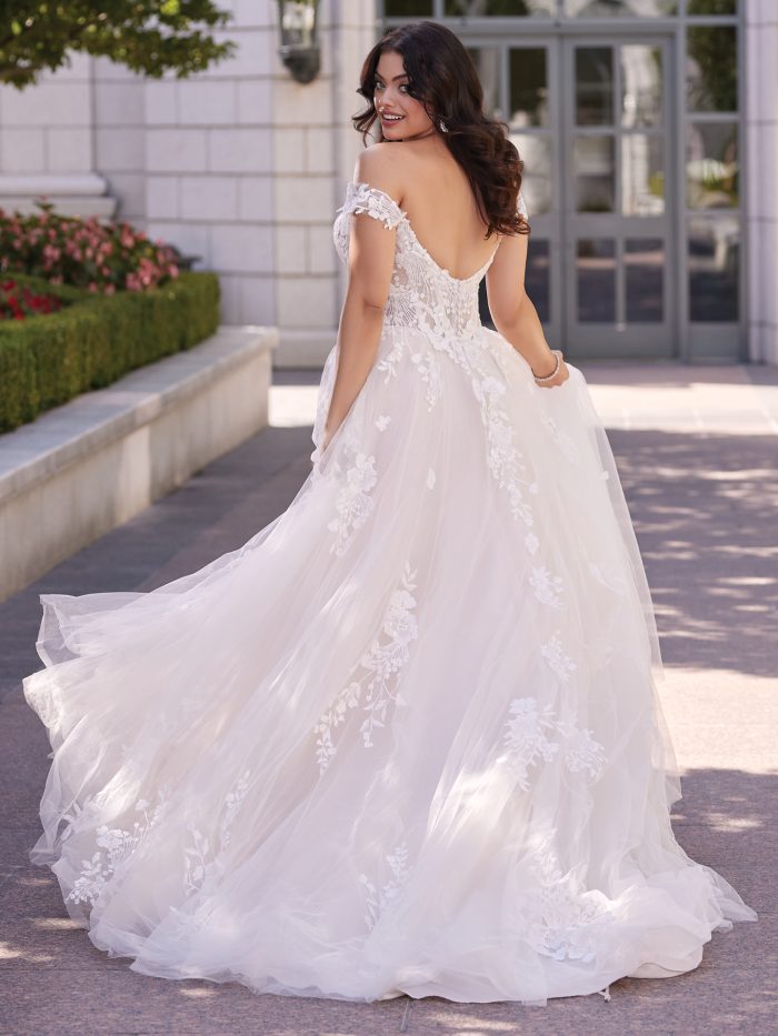 Back view of Harlem by Maggie Sottero showcasing the soft V-back, illusion lace bodice, off-the-shoulder lace cap sleeves, and flowing tulle train with floral lace detailing.