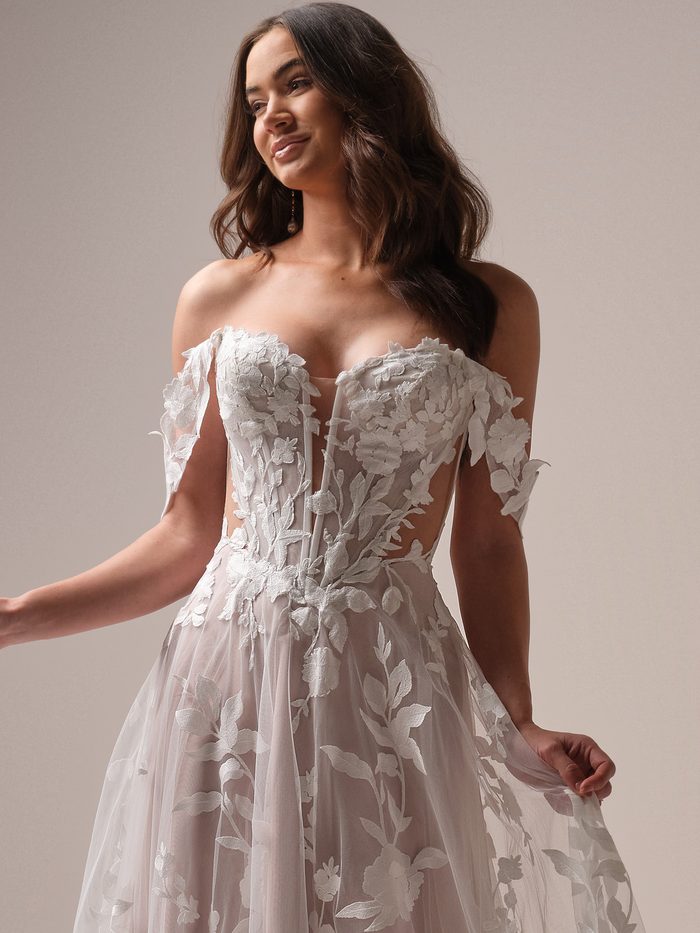 Natalie boho floral A-line wedding dress with detachable off-the-shoulder sleeves, featuring oversized floral appliqués, a sheer corset bodice, and dimensional botanical embroidery for a romantic bridal look.
