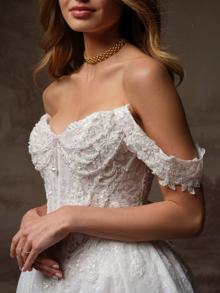 Close-up of Maggie Sottero Ryland wedding gown featuring a strapless lace bodice with pearl and sequin embellishments and delicate off-the-shoulder lace sleeves.