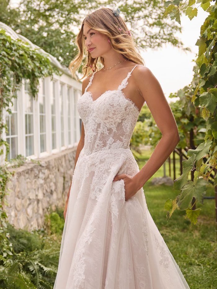Esmeralda boho floral A-line wedding dress with floral lace appliqués, lace straps, a sheer corset-inspired bodice, and a flowing tulle skirt with hidden pockets.