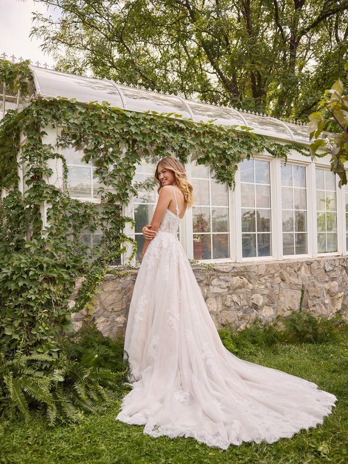 Back view of the Esmeralda boho floral A-line wedding dress featuring delicate lace straps, a soft tulle skirt, floral lace appliqués, and a sweeping train in a garden-inspired setting.