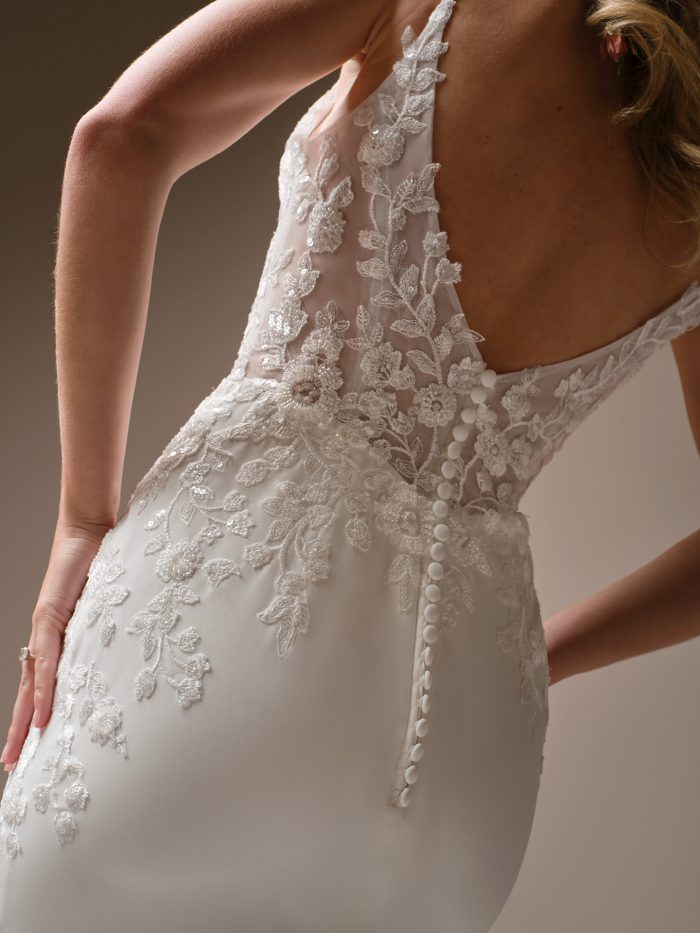 Close-up of the back of a sheath wedding dress with illusion lace detailing and covered buttons. The floral lace appliqués trail down from the sheer bodice, highlighting the gown’s romantic texture and sleek, fitted silhouette.