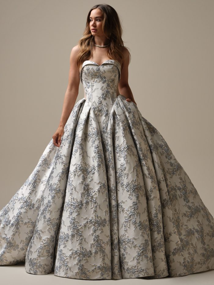 Bride wearing Aberdeen by Sottero and Midgley, a blue floral jacquard ballgown wedding dress featuring a strapless sweetheart neckline, drop waist bodice, and full dramatic skirt with pockets.