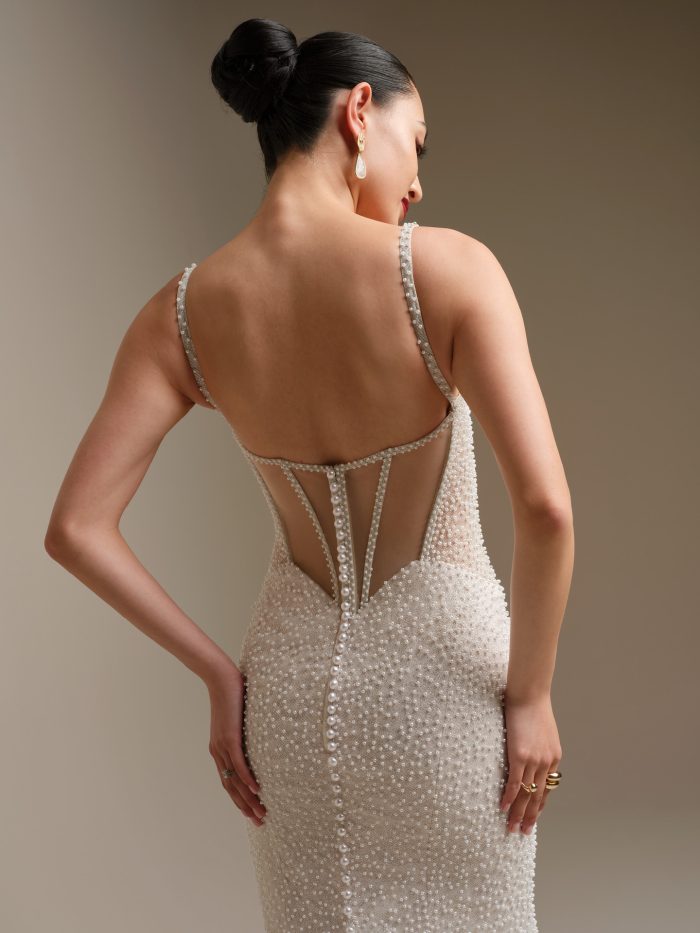 Alt text: “Back view of Sottero and Midgley Cooper pearl-beaded sheath wedding dress with illusion back detail, spaghetti straps, and fabric-covered buttons trailing down the skirt.”