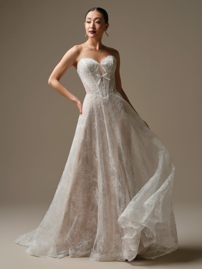 Bride wearing Granger by Sottero and Midgley, a strapless Chantilly lace A-line wedding dress with exposed boning, bow detail at the neckline, and soft sweetheart bodice, shown in ivory over blush.