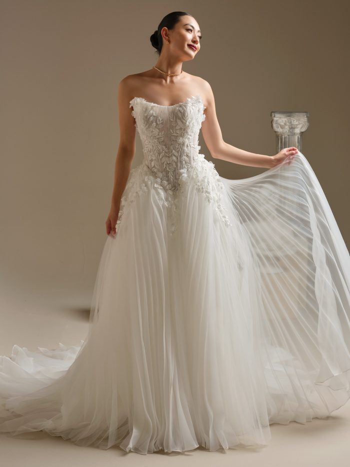 Bride wearing Jayna by Sottero and Midgley, a strapless tulle ball gown with a pleated skirt, illusion corset bodice, and 3D floral lace detailing.