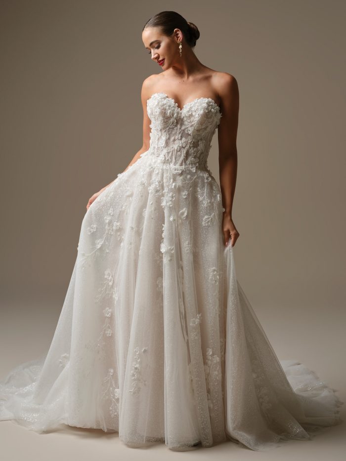 Bride wearing a strapless ballgown wedding dress featuring a sweetheart neckline, sheer corset bodice, and 3-D floral lace appliqués. The gown’s layered tulle skirt sparkles with subtle shimmer for a romantic and modern bridal look.