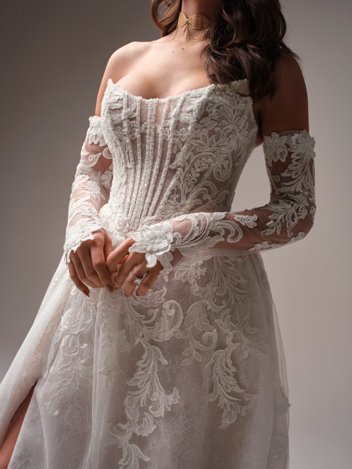 Close-up of Sottero and Midgley Parker A-line wedding dress featuring exposed boning, embroidered lace motifs, and detachable off-the-shoulder illusion sleeves