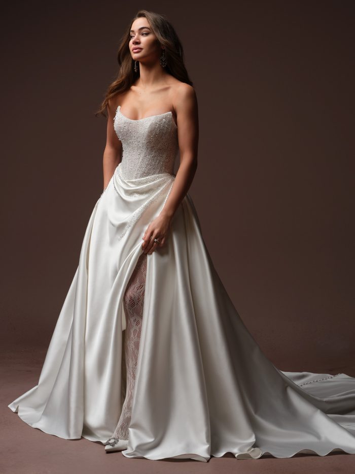 Full-length view of Sottero and Midgley Rumi ballgown wedding dress with a strapless beaded bodice, draped satin skirt with a high side slit, and a chapel-length train.