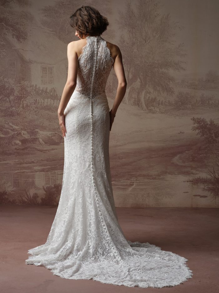 Back view of a bride wearing the Anya lace sheath wedding dress, showing a sheer illusion lace back with a row of covered buttons from the halter neckline down to the fitted skirt and train.