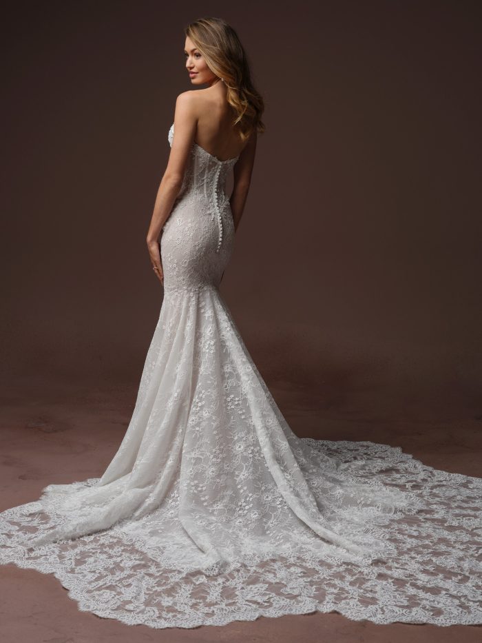 Back view of a bride wearing the Bellevue Royale strapless fit-and-flare wedding dress in lace, showing a row of covered buttons down the low back and a dramatic lace train.