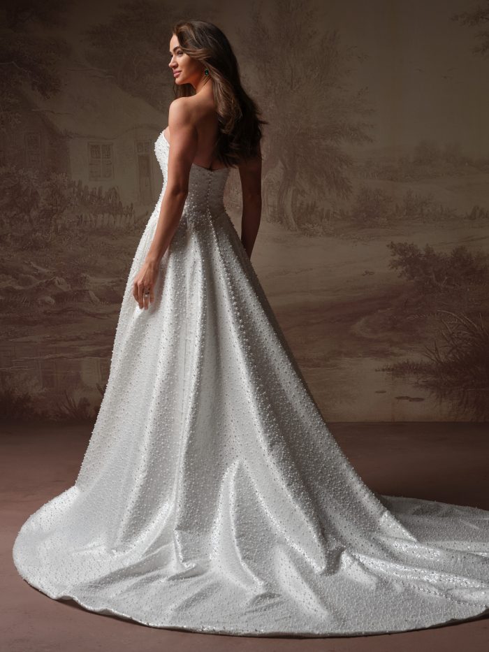 Side/back view of a bride wearing the Elowyn A-line wedding dress, showing the pearl beading detail along the fitted strapless bodice and the sweeping train of the A-line skirt.