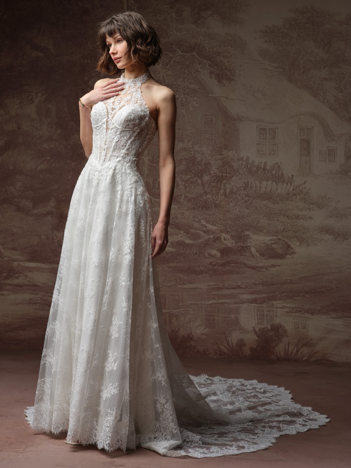 Front/side view of a bride wearing the Lucca Marie A-line wedding dress in lace, featuring a beaded high halter neckline with a sheer illusion bodice and a flowing lace skirt with lace-trimmed train.