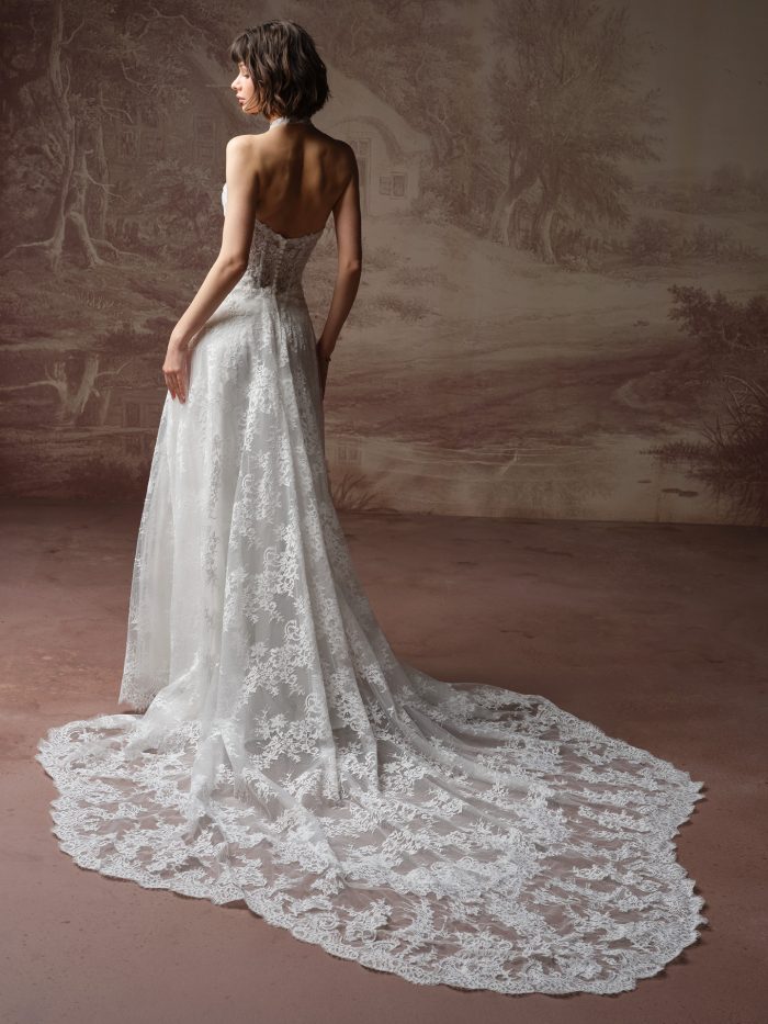 Back view of a bride wearing the Lucca Marie A-line wedding dress, showing an open back with a halter neckline and a delicate lace A-line skirt sweeping into a scalloped lace train.