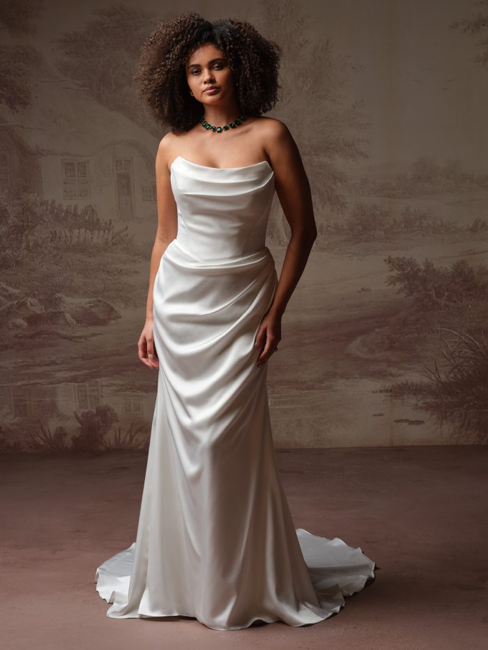 Front view of a bride wearing the Prestyn sheath wedding dress in satin, featuring a strapless draped cowl neckline, ruched hip detail, and a sleek fitted skirt with train.