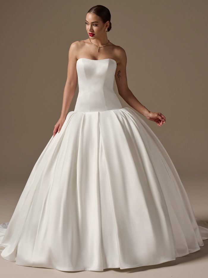 Front view of a bride wearing the Adair wedding dress in satin, featuring a strapless structured bodice with a dropped waist and a voluminous pleated ballgown skirt with train.