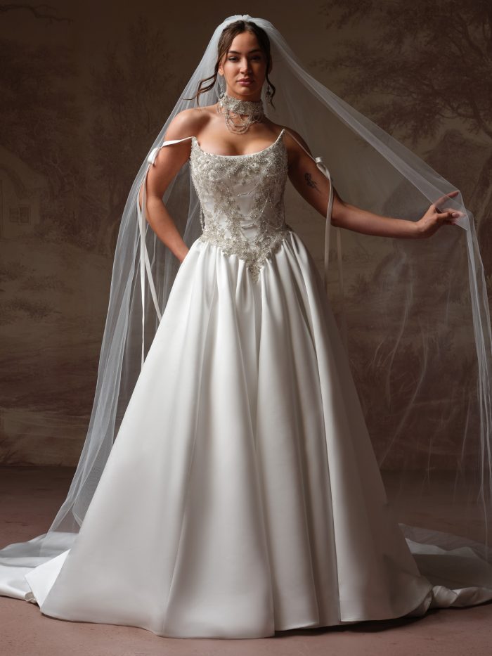 Plus-size bride wearing the Aelarion A-line wedding dress in satin, featuring a beaded bodice with draped crystal detailing, tie-strap shoulders, and a full satin skirt with cathedral veil.