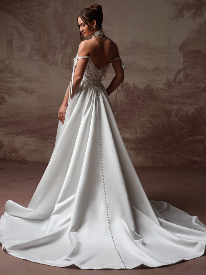 Back view of a plus-size bride wearing the Aelarion A-line wedding dress, showing an off-the-shoulder tie-strap beaded bodice with a row of covered buttons down the satin skirt and sweeping train.