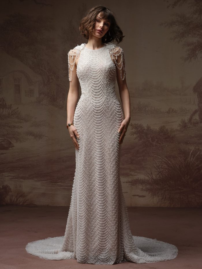 Front view of a bride wearing the Oleta sheath wedding dress, featuring an allover beaded high-neck bodice with a scalloped scallop-drape pattern, sheer beaded shoulder cascades, and a fitted skirt with train.