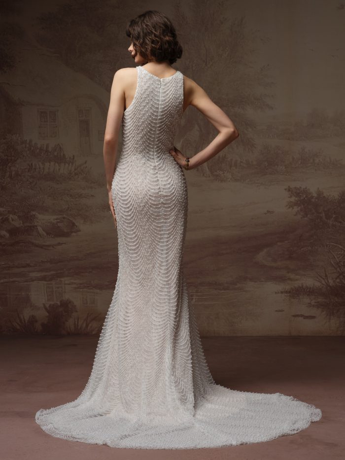 Back view of a bride wearing the Oleta sheath wedding dress, showing a high round neckline and fitted allover beaded bodice with a scalloped drape pattern flowing into a sleek train.